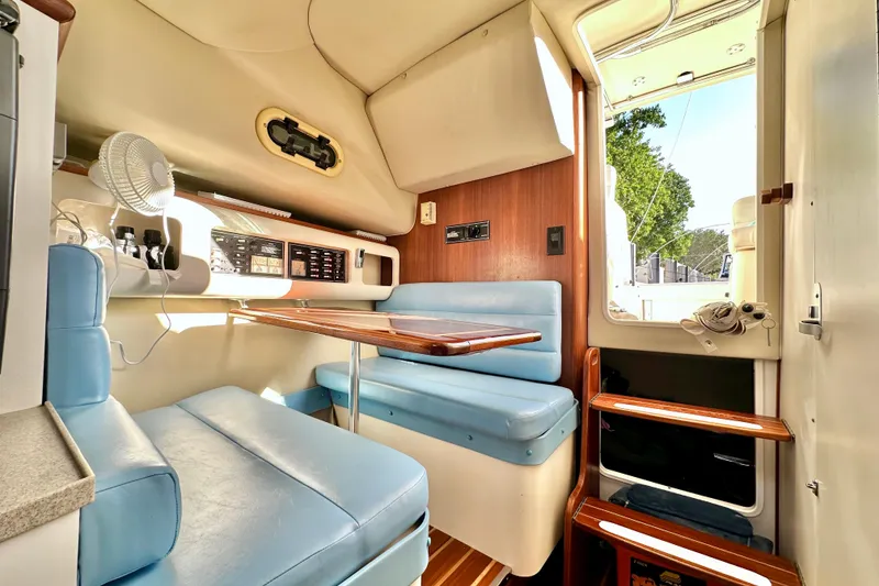 Slide: The Image of 2004 Pursuit 3070 Offshore cabin interior with blue seating and wooden table. - 66