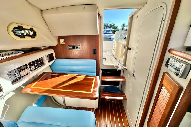 Slide: The Image of 2004 Pursuit 3070 Offshore cabin interior with blue seating and wooden table. - 68