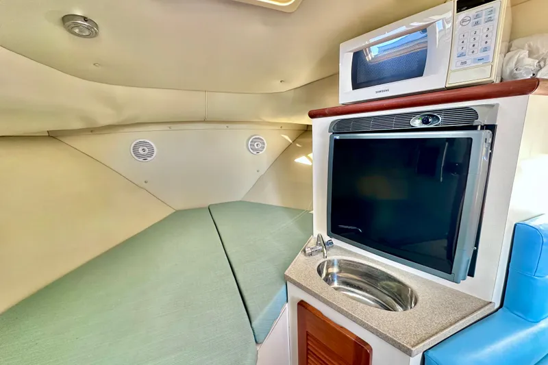 Slide: The Image of 2004 Pursuit 3070 Offshore cabin with kitchenette, featuring a microwave, sink, and compact fridge. - 88