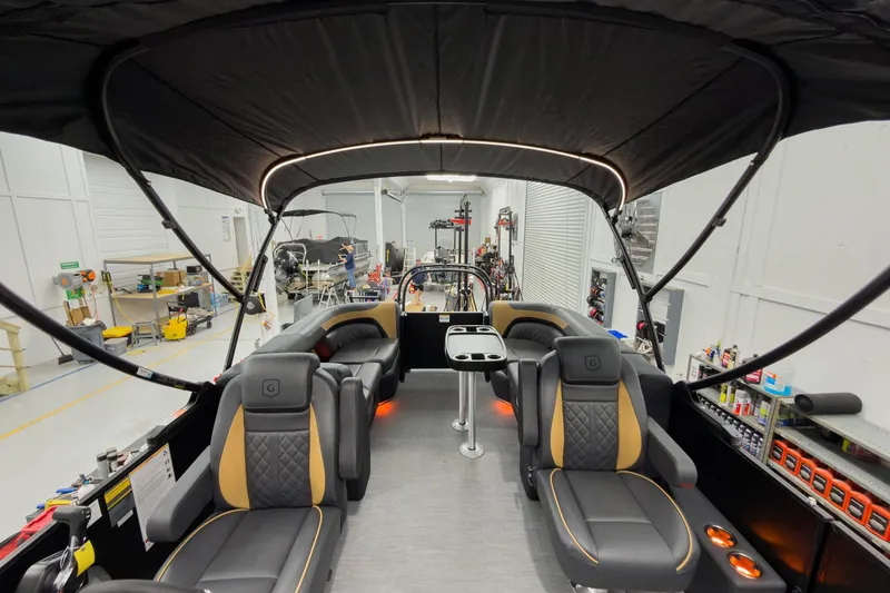 Slide: The Image of 2026 Godfrey Sweetwater 22' Tritoon interior with luxurious seating and canopy in a workshop. - 35