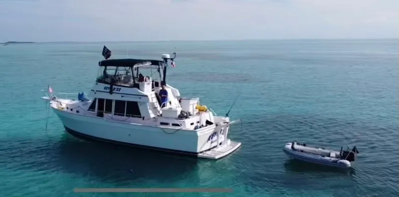 Slide: The Image of 1999 Mainship 430 Trawler anchored in clear blue water with a small dinghy nearby. - 1