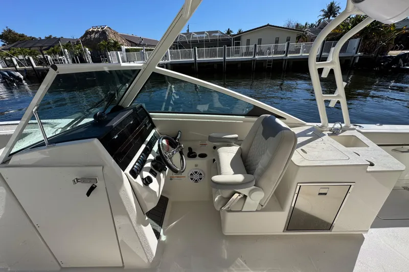 Slide: The Image of 2025 Sailfish 276 DC boat cockpit with steering wheel and seating, dockside view. - 12