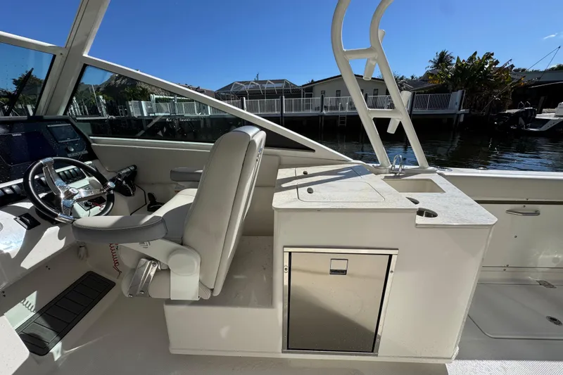 Slide: The Image of 2025 Sailfish 276 DC boat interior with helm, seating, and storage, docked by waterfront homes. - 19