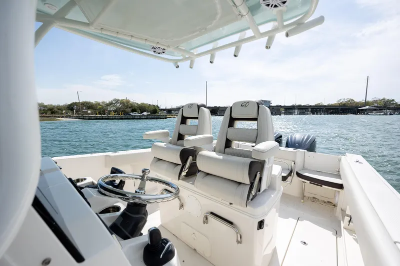 Slide: The Image of 2024 Sailfish 290 CC boat interior with dual captain's chairs and steering wheel on open water. - 21