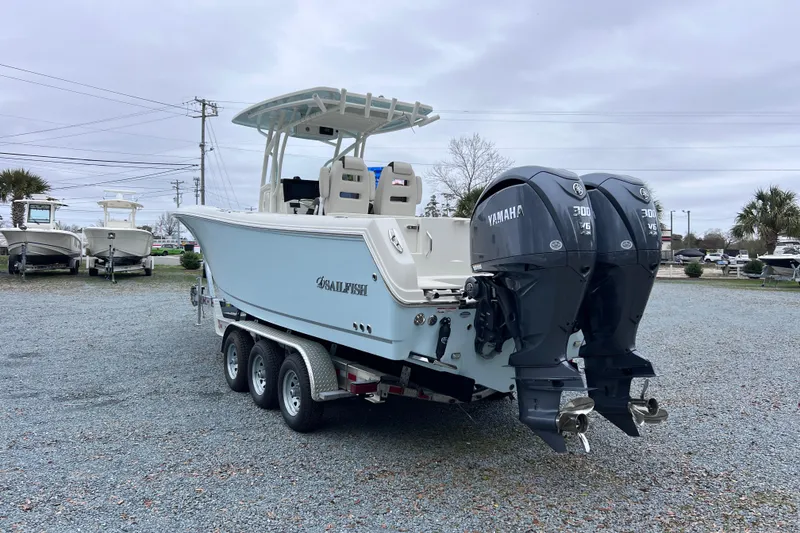Slide: The Image of 2024 Sailfish 290 CC boat on trailer, parked outdoors with trees in background. - 6