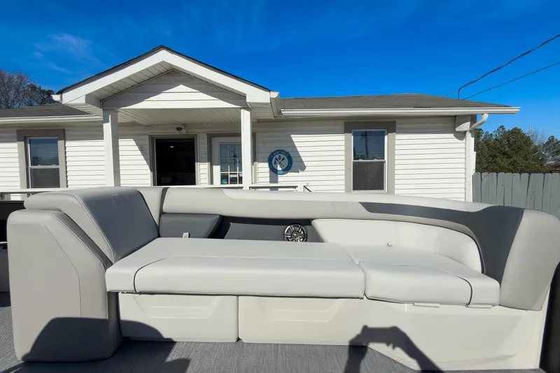 Slide: The Image of 2026 Godfrey Sweetwater 22' Split Bench Tritoon with sleek seating, parked near a white house. - 31