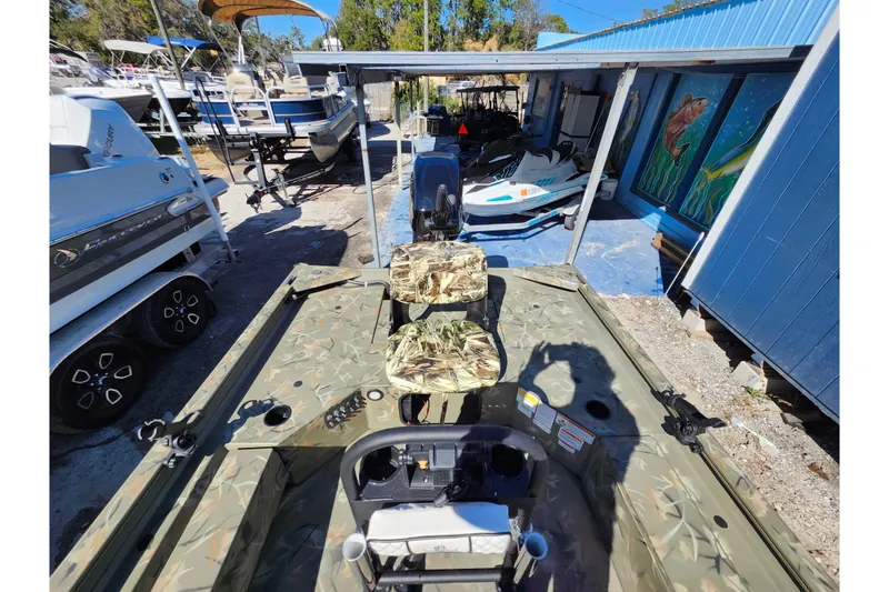 Slide: The Image of 2025 Tracker Grizzly 1654 MVX Sportsman boat with camouflage seats, parked outdoors. - 30