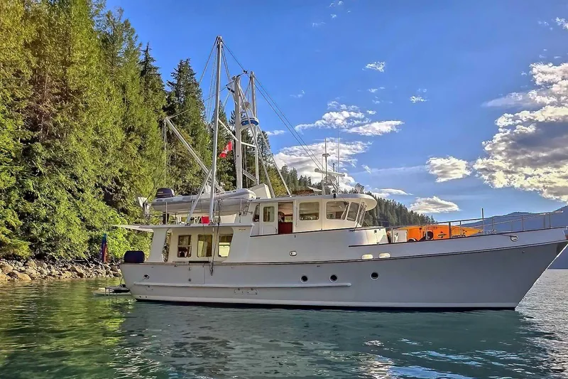 Slide: The Image of Nordhavn 46 yacht from 2001 on serene water, surrounded by lush forest and clear sky. - 69