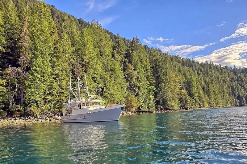 Slide: The Image of Nordhavn 46 yacht from 2001 anchored near lush forested shoreline under blue sky. - 72