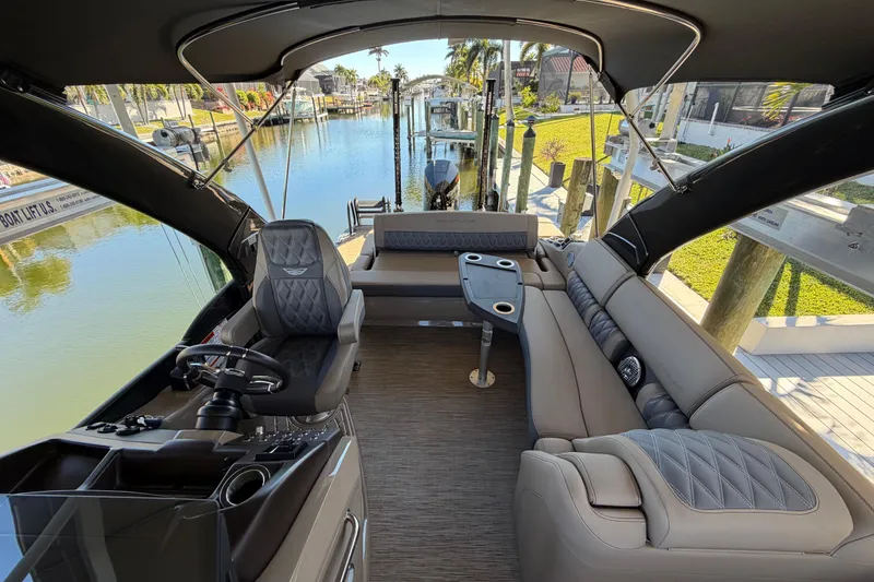 Slide: The Image of 2024 Bennington 25 QX Swingback interior with luxurious seating and modern helm, docked by a canal. - 12