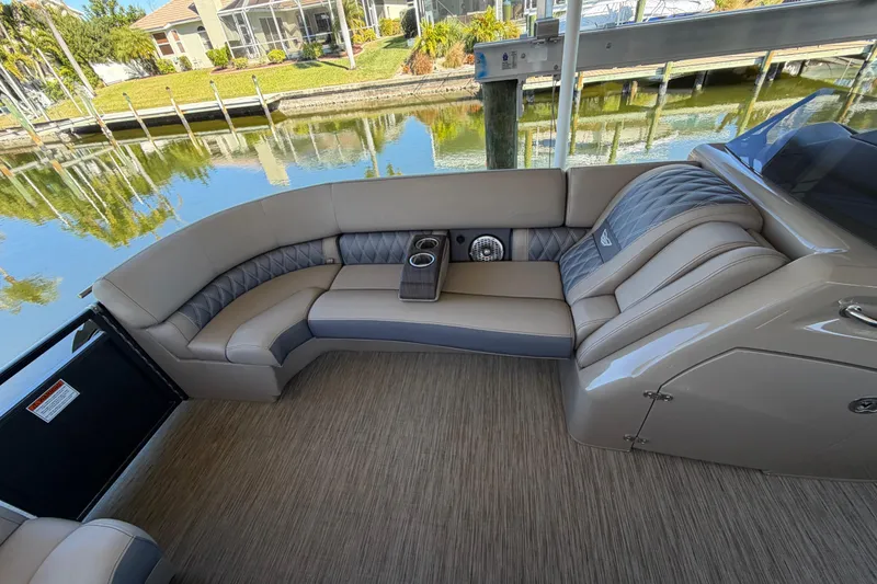 Slide: The Image of 2024 Bennington 25 QX Swingback interior with luxurious seating and cup holders by a serene waterfront. - 18