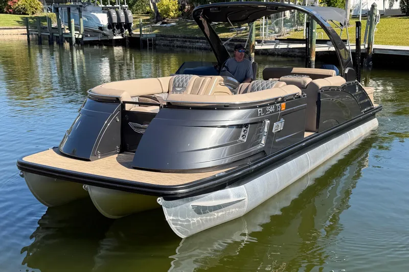 Slide: The Image of 2024 Bennington 25 QX Swingback pontoon boat on calm water, featuring luxurious seating. - 2