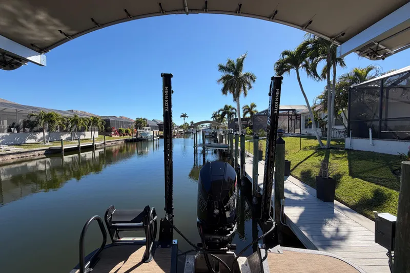 Slide: The Image of 2024 Bennington 25 QX Swingback on a serene canal with palm trees and docks. - 26