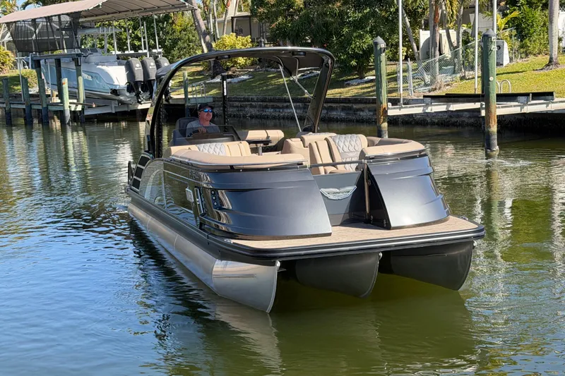 Slide: The Image of 2024 Bennington 25 QX Swingback pontoon boat on calm water near a dock. - 7