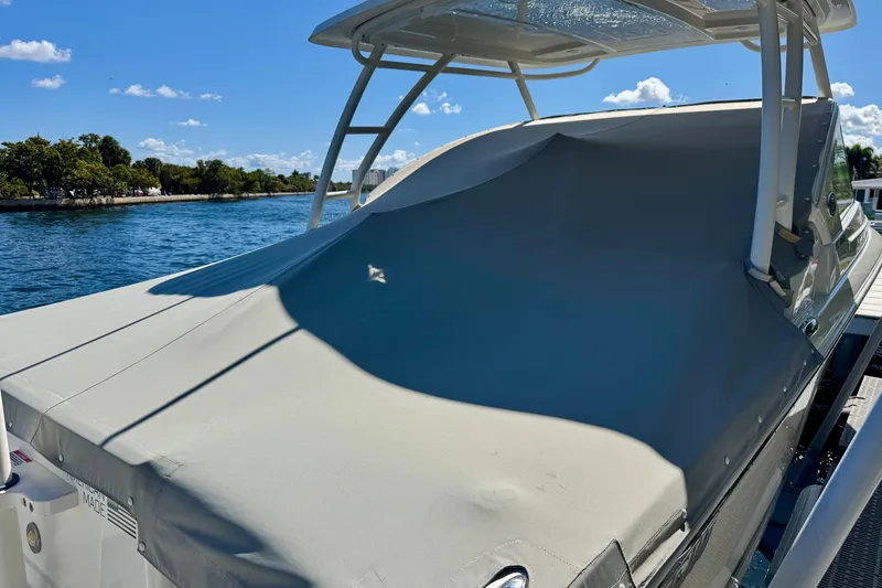 Slide: The Image of 2020 Pursuit DC 266 Dual Console boat covered, docked by a scenic waterfront. - 20