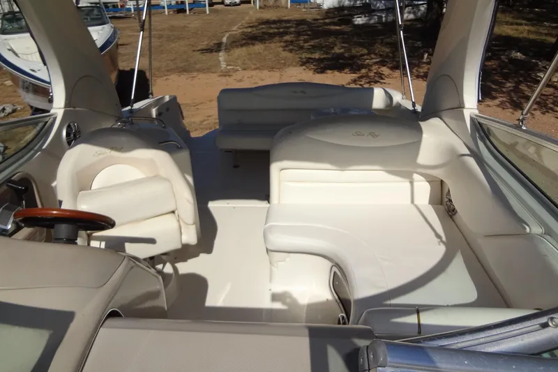 Slide: The Image of 2002 Sea Ray Sundancer 280 interior with white seating and steering wheel, docked on sandy shore. - 12