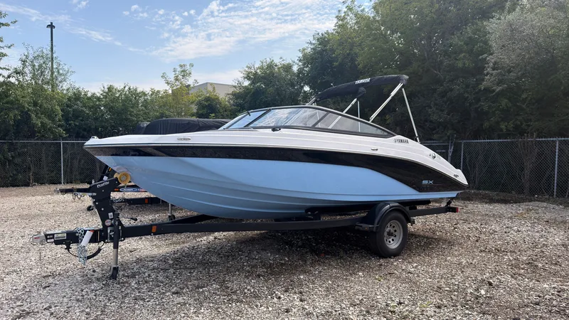 The Image of Yamaha SX195 2026: Sleek motorboat with a blue hull, on a trailer, surrounded by trees. - 0