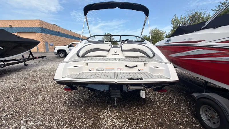 Slide: The Image of The image shows a 2026 Yamaha SX195 boat with a black bimini top, parked on a gravel lot. - 2