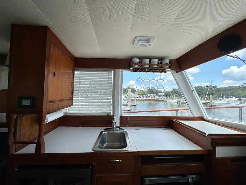 Slide: The Image of 1974 Grand Banks 32 Sedan interior with sink, wooden cabinetry, and marina view through large windows. - 25