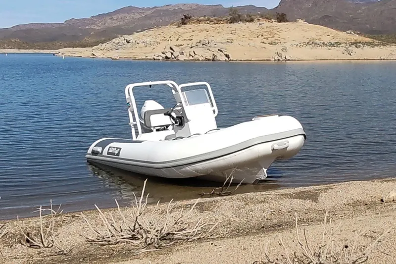 Slide: The Image of Manufacturer Provided Image: 2025 Tide Craft Beaver 10 inflatable boat on a sandy lakeshore with mountainous backdrop. - 2
