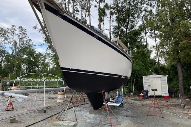 Slide: The Image of 1988 Caliber 38 sailboat on stands in a boatyard, surrounded by trees and equipment. - 12