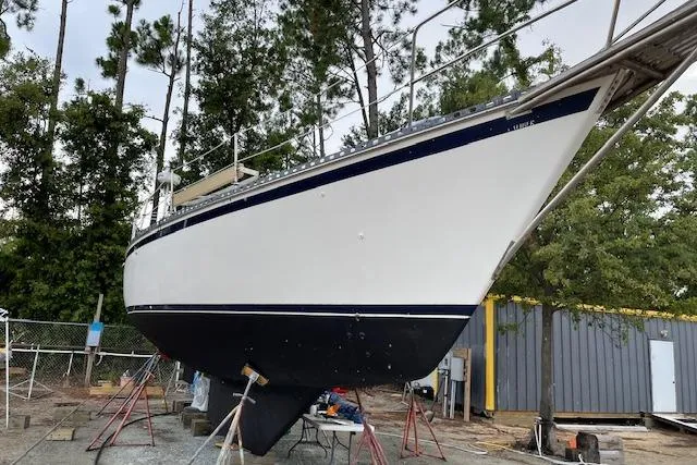 Slide: The Image of 1988 Caliber 38 sailboat on stands, surrounded by trees and storage buildings. - 13