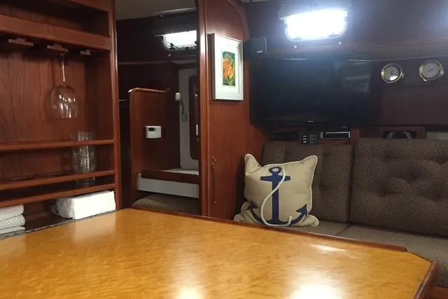 Slide: The Image of 1988 Caliber 38 yacht interior with wood finish, anchor-themed pillow, and cozy seating area. - 2
