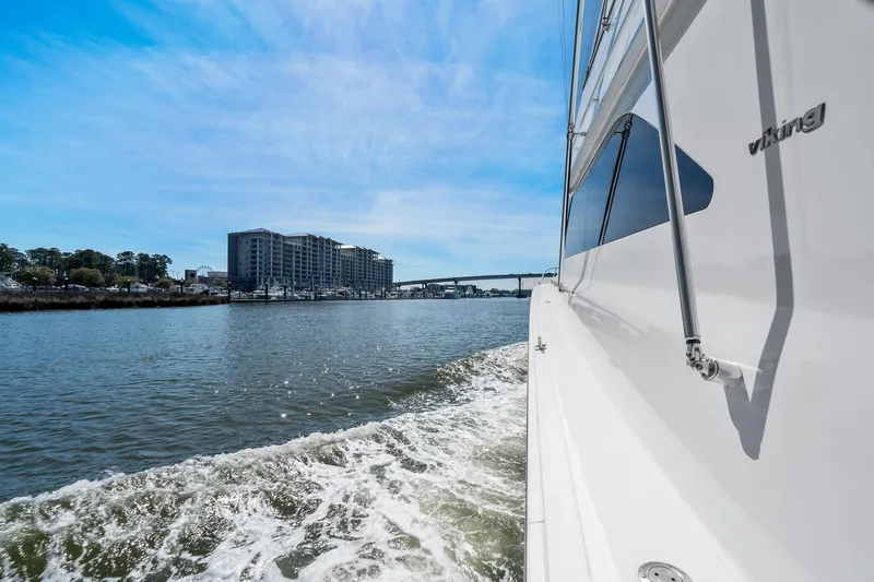 Slide: The Image of 2002 Viking 61 Convertible yacht cruising near waterfront buildings under a clear blue sky. - 44