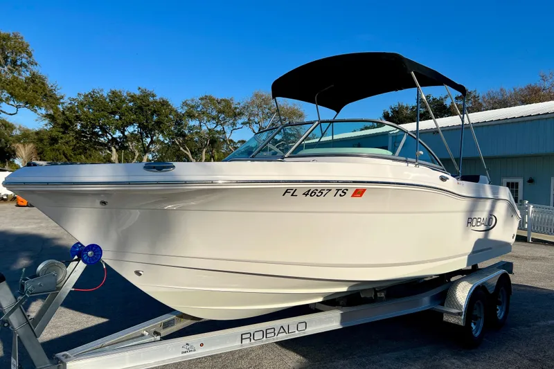Slide: The Image of 2024 Robalo R207 Dual Console boat on trailer, parked outdoors under clear blue sky. - 2