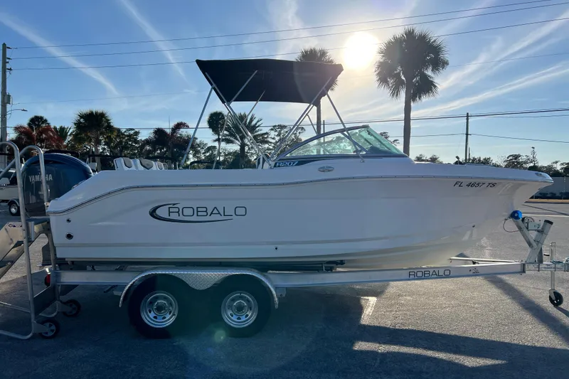 Slide: The Image of 2024 Robalo R207 Dual Console boat on trailer, sunny day, palm trees in background. - 6