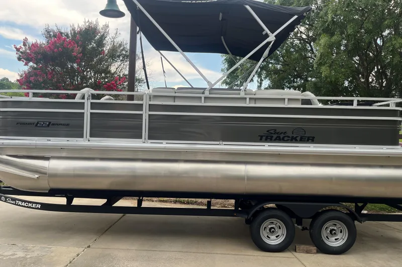Slide: The Image of 2026 Sun Tracker Fishin' Barge 22 DLX pontoon boat on trailer, parked outdoors. - 2