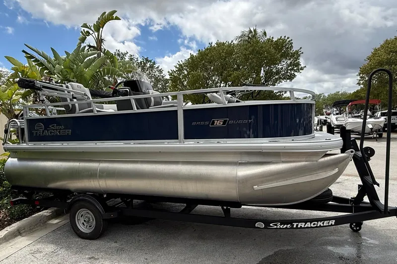 The Image of 2026 Sun Tracker Bass Buggy 16 XL Select pontoon boat on trailer, parked outdoors. - 0