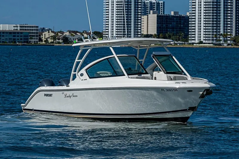 Slide: The Image of 2022 Pursuit DC 266 Dual Console boat cruising on water with city skyline backdrop. - 19