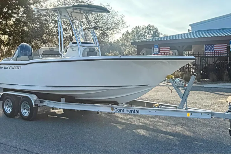 Slide: The Image of 2026 Key West 203 FS boat on trailer, parked outdoors with American flags in background. - 1