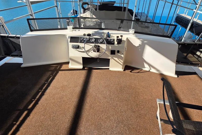 Slide: The Image of 1999 Stardust Cruisers 16x60 houseboat helm with steering wheel and controls, docked on calm water. - 16
