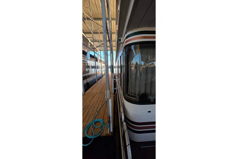 Slide: The Image of 1999 Stardust Cruisers 16x60 houseboat docked, featuring wooden deck and marina setting. - 24