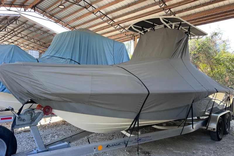 Slide: The Image of 2021 NauticStar 227 XTS boat covered and stored on a trailer under a metal roof. - 2