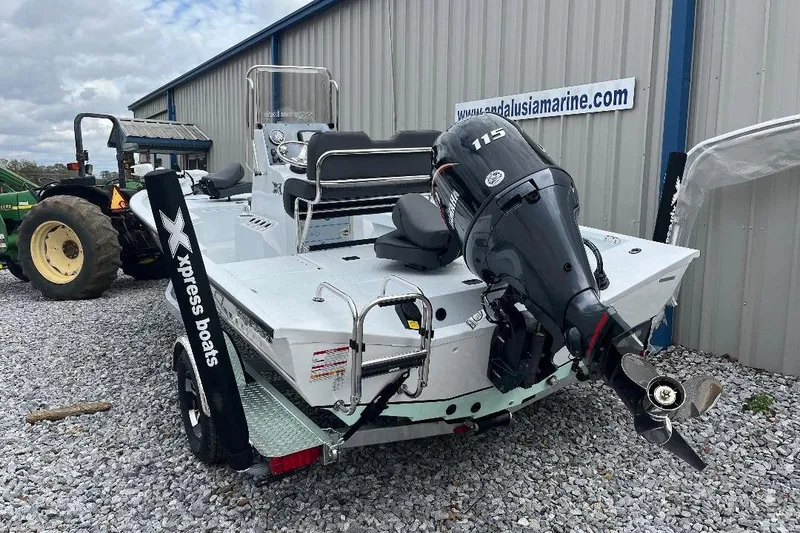 Slide: The Image of 2026 Xpress H20B Bay boat with outboard motor, parked on gravel near a building. - 9