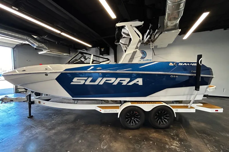 The Image of 2025 Supra SA boat on trailer in showroom, blue and white design. - 0