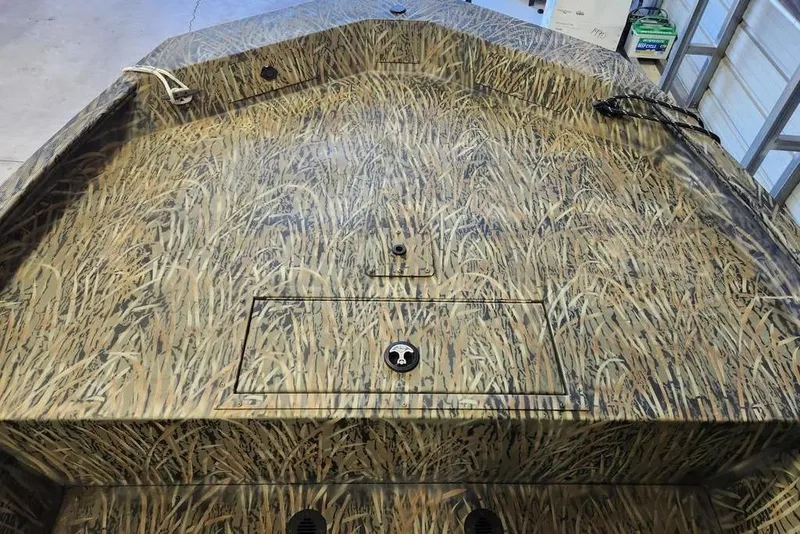 Slide: The Image of 2025 Tracker Grizzly 1860 CC boat with camouflage pattern in a garage setting. - 10