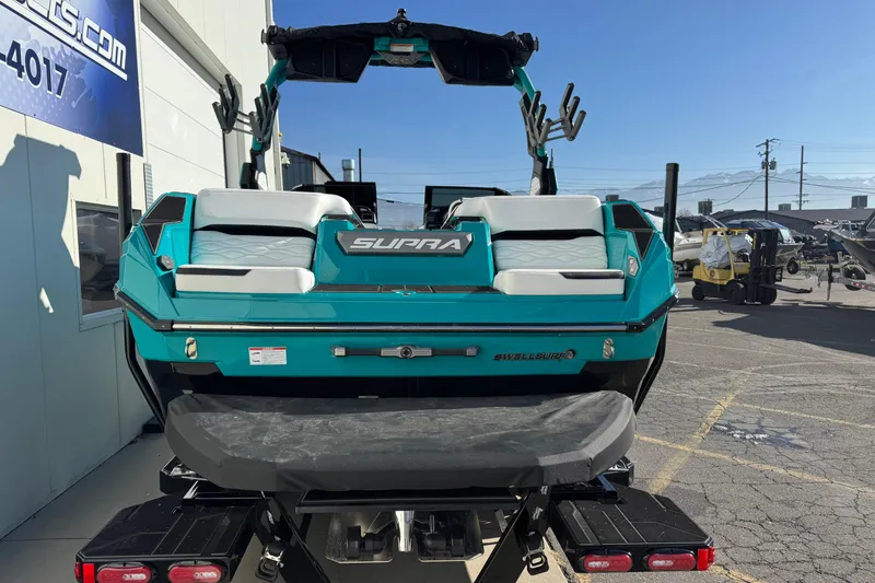 Slide: The Image of 2026 Supra SA 575 boat, teal color, rear view, parked outdoors. - 4
