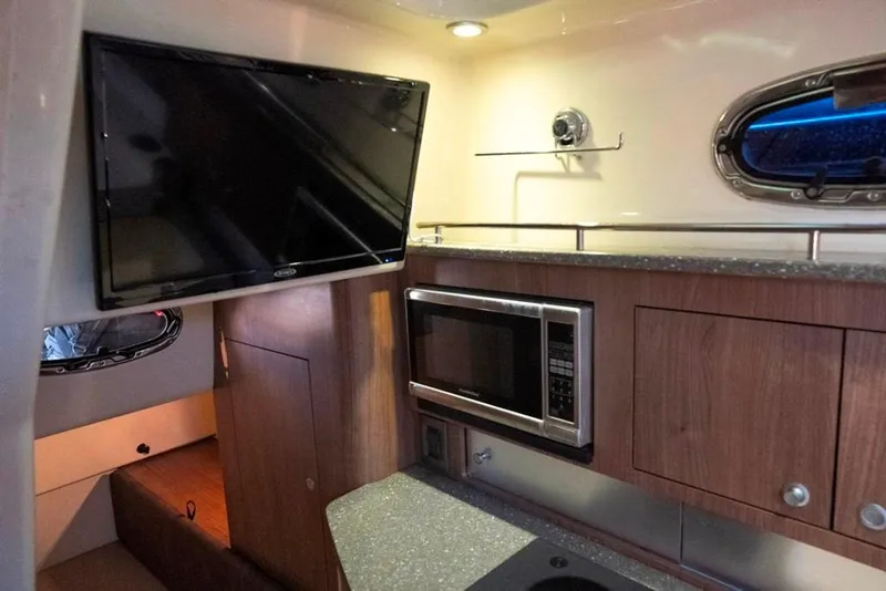 Slide: The Image of 2014 Boston Whaler 315 Conquest interior with TV, microwave, and wood cabinetry. - 37