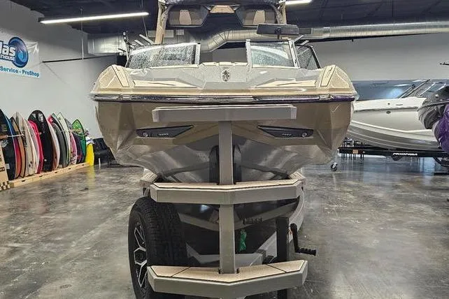 Slide: The Image of 2026 Supra SL boat in showroom, front view with trailer, surrounded by surfboards. - 6