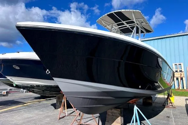 The Image of 2020 Cobia 237 Center Console boat on stands, black hull, blue sky background. - 0