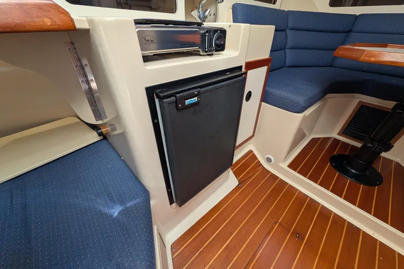 Slide: The Image of 2004 Albin 30 Family Cruiser interior with fridge, blue seating, and wood flooring. - 2