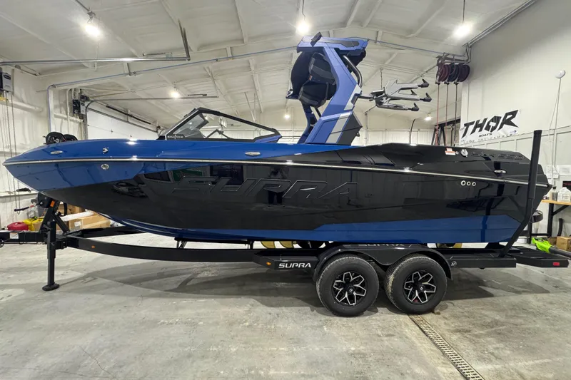 The Image of 2026 Supra SL boat in a garage, featuring sleek black and blue design on a trailer. - 1