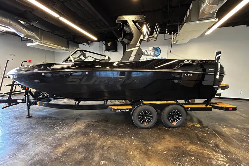 The Image of 2025 Supra SL boat in showroom, sleek black design on trailer. - 1