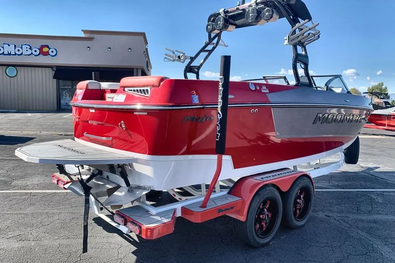 Slide: The Image of 2023 Moomba Mojo boat in red and gray on a trailer, parked outside a building. - 5