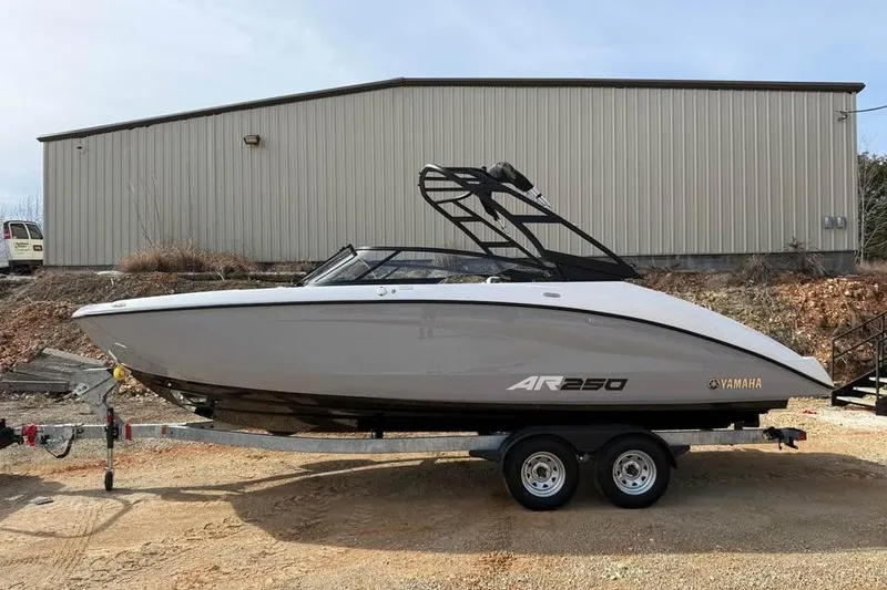 The Image of 2026 Yamaha Boats AR250 on trailer, parked outdoors near a warehouse. - 0