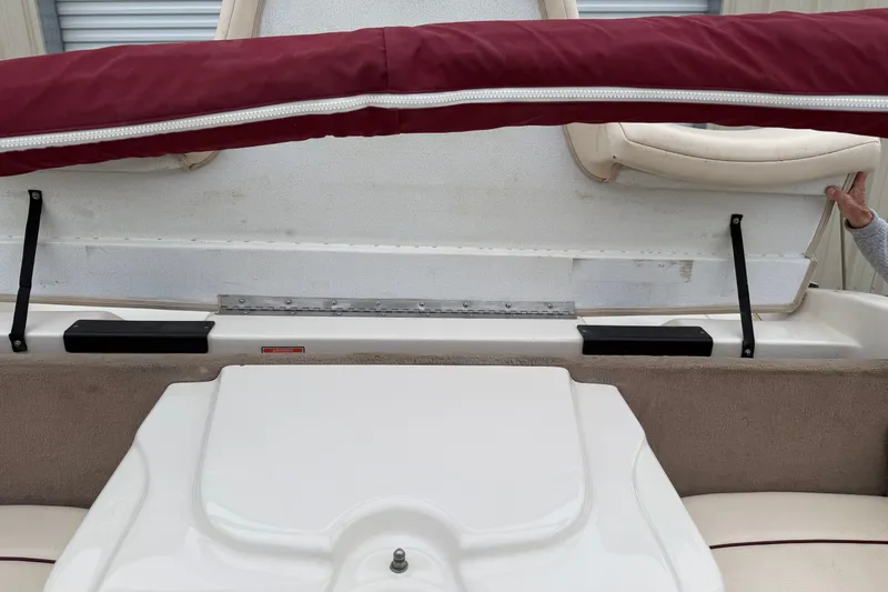 Slide: The Image of 2000 Sea Ray 210 Bow Rider interior storage compartment with maroon cover and beige seating. - 8